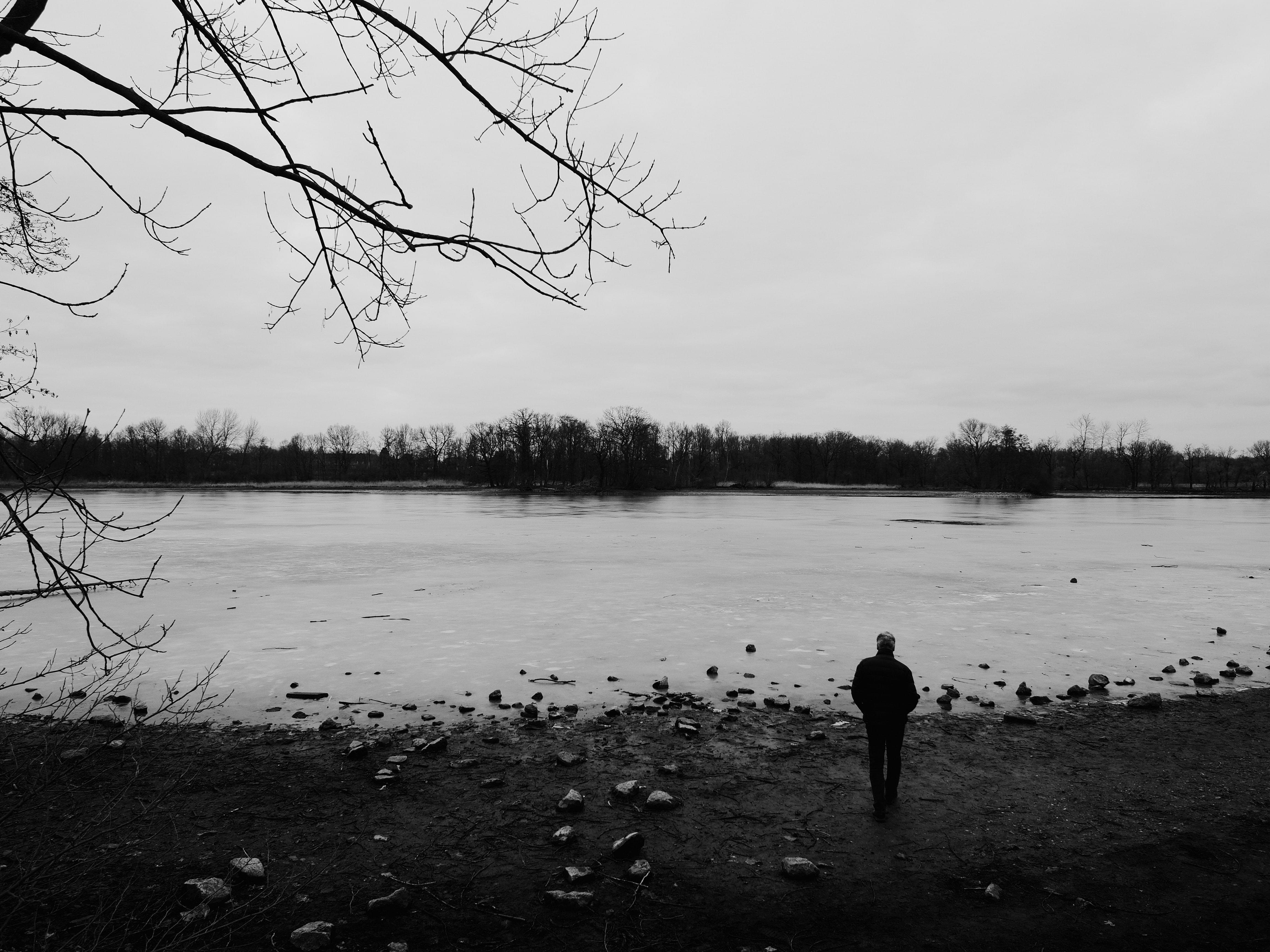 The back of a man overlooking an almost frozen pond in black and white