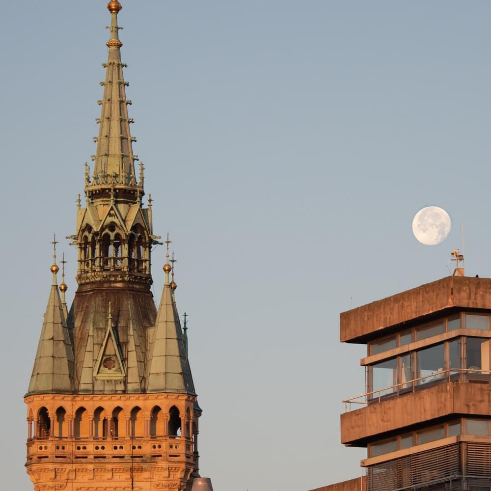 The moon rises in the morning over the new town hall next to the tower of the old town hall