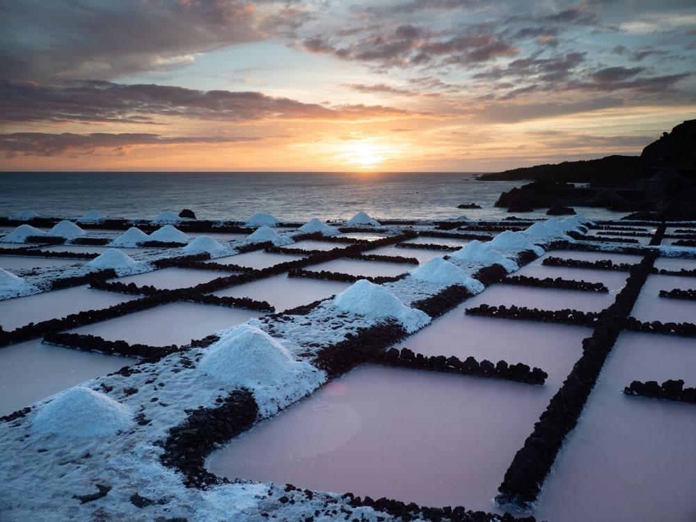 Pink sea water pools in a salination plant in front of an orange sunset